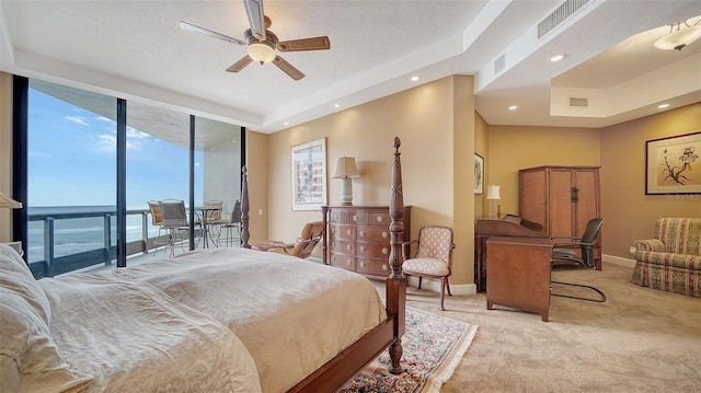 bedroom featuring a wall of windows, light colored carpet, a water view, ceiling fan, and access to exterior