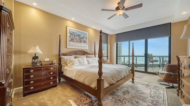 carpeted bedroom with ceiling fan, a tray ceiling, access to exterior, and a water view