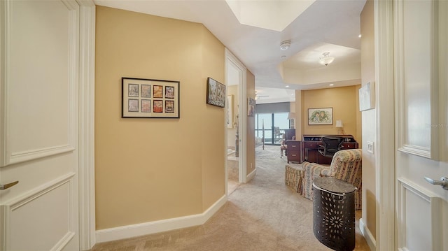 corridor featuring a raised ceiling and light carpet