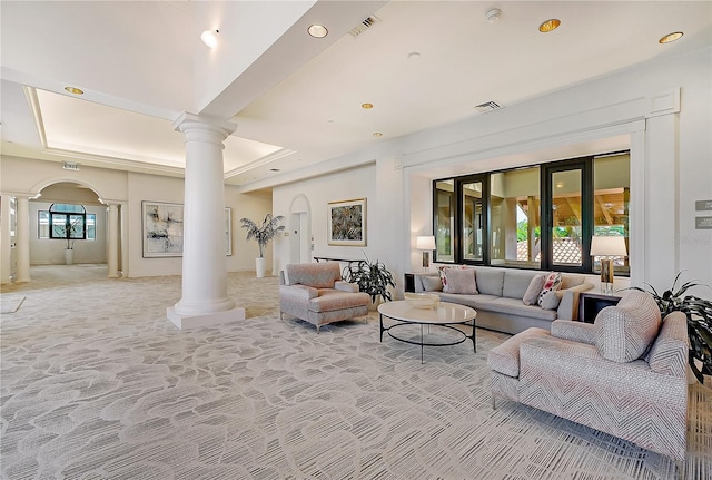 living room with ornate columns, a raised ceiling, and light carpet