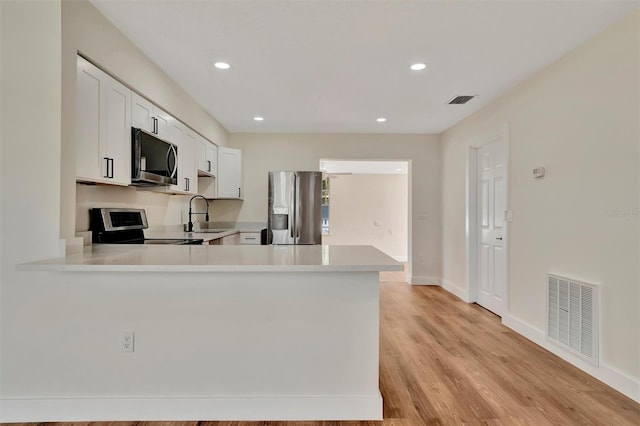 kitchen with kitchen peninsula, stainless steel appliances, light hardwood / wood-style floors, white cabinets, and sink