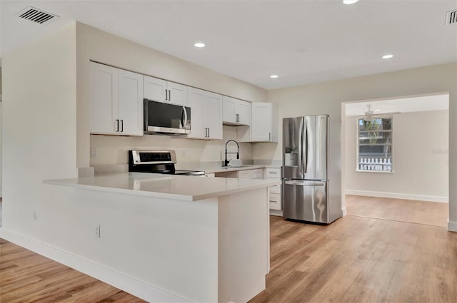 kitchen featuring sink, white cabinetry, light wood-type flooring, kitchen peninsula, and appliances with stainless steel finishes