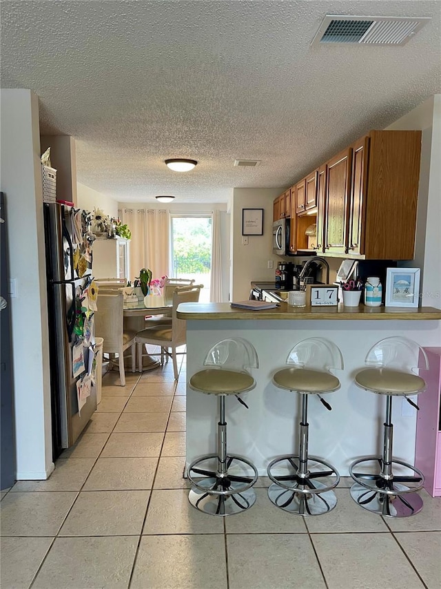 kitchen with a kitchen breakfast bar, light tile patterned floors, kitchen peninsula, and appliances with stainless steel finishes