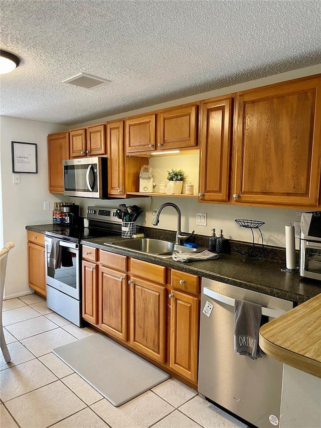 kitchen featuring sink, a textured ceiling, appliances with stainless steel finishes, and light tile patterned flooring