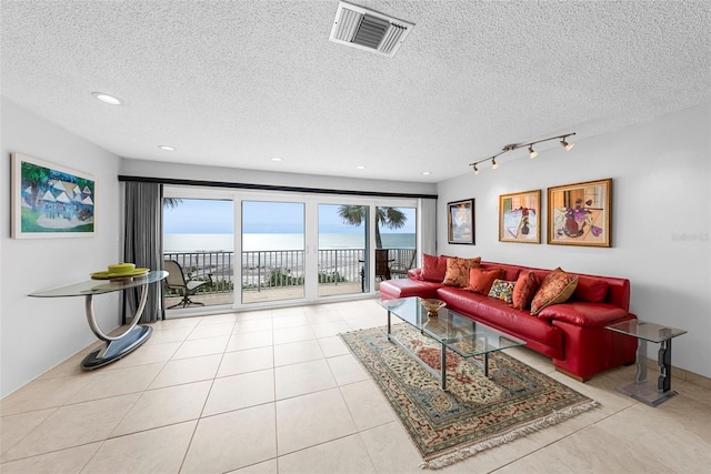 tiled living room with a textured ceiling, track lighting, and a water view