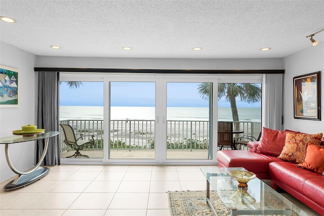 tiled living room with rail lighting, a textured ceiling, and a water view