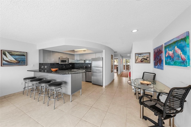 kitchen featuring backsplash, gray cabinets, appliances with stainless steel finishes, a textured ceiling, and light tile patterned floors