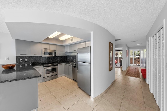 kitchen featuring appliances with stainless steel finishes, dark stone counters, tasteful backsplash, light tile patterned floors, and gray cabinetry