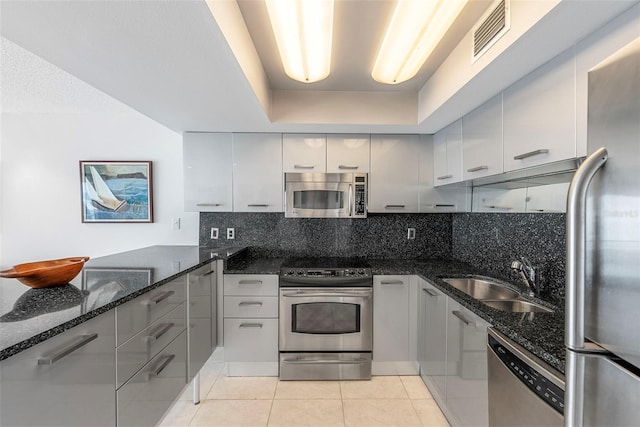 kitchen with light tile patterned floors, appliances with stainless steel finishes, tasteful backsplash, dark stone counters, and sink