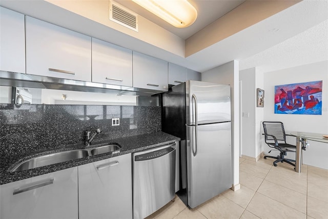 kitchen with stainless steel appliances, tasteful backsplash, dark stone countertops, sink, and light tile patterned floors