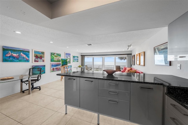 kitchen with a textured ceiling, dark stone counters, kitchen peninsula, light tile patterned flooring, and gray cabinetry