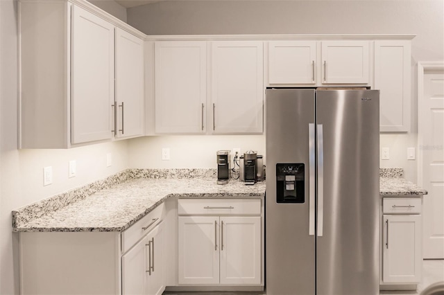 kitchen with white cabinetry, stainless steel fridge, and light stone counters