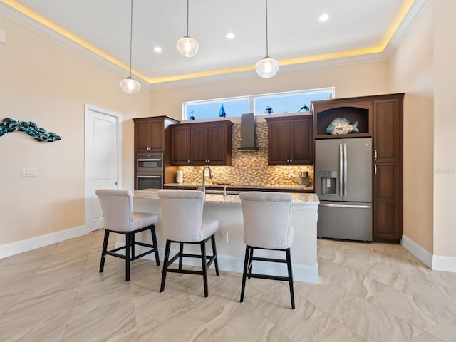 kitchen featuring pendant lighting, appliances with stainless steel finishes, wall chimney exhaust hood, light stone counters, and a center island with sink