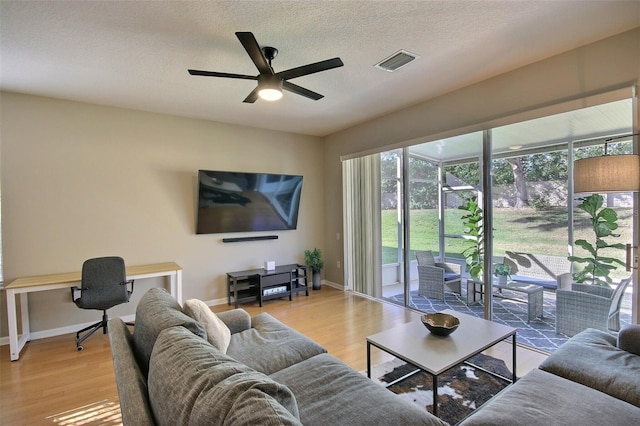 living room featuring light hardwood / wood-style floors, a textured ceiling, and ceiling fan