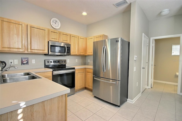 kitchen featuring a textured ceiling, appliances with stainless steel finishes, light brown cabinets, sink, and light tile patterned floors