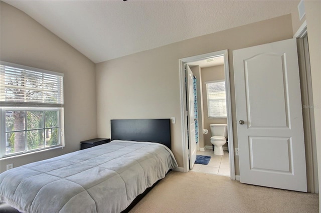 carpeted bedroom featuring vaulted ceiling, ensuite bathroom, and multiple windows