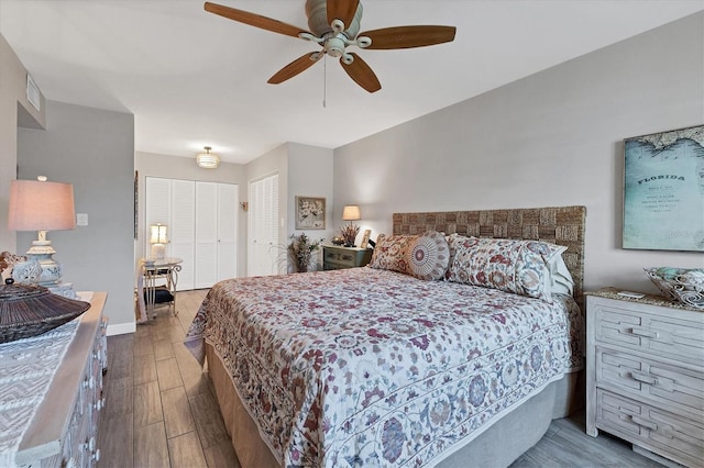 bedroom with a ceiling fan, visible vents, baseboards, and wood finished floors