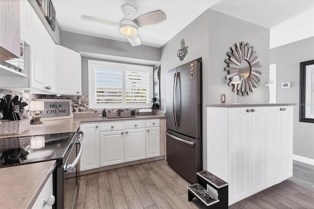 kitchen with white cabinets, a sink, stainless steel appliances, light wood-style floors, and backsplash