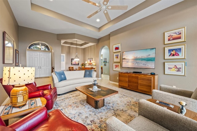 tiled living room with ceiling fan and a raised ceiling