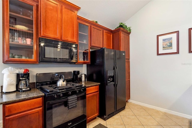 kitchen with black appliances, dark stone counters, vaulted ceiling, and light tile patterned floors