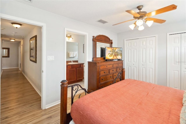 bedroom featuring ceiling fan, light hardwood / wood-style flooring, multiple closets, and ensuite bath