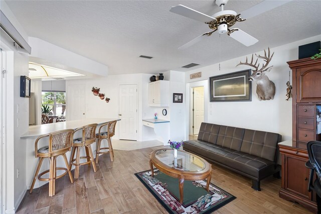 living room featuring a textured ceiling, light wood-type flooring, and ceiling fan