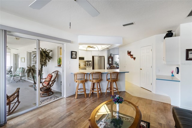 interior space with light hardwood / wood-style flooring, stainless steel fridge, white cabinetry, and kitchen peninsula