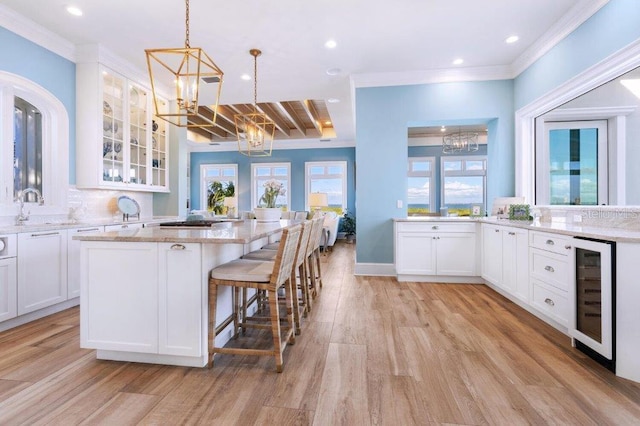 kitchen featuring white cabinetry, beverage cooler, hanging light fixtures, and light stone counters