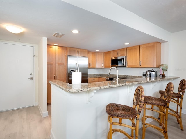 kitchen featuring a breakfast bar, appliances with stainless steel finishes, light hardwood / wood-style floors, light stone countertops, and kitchen peninsula