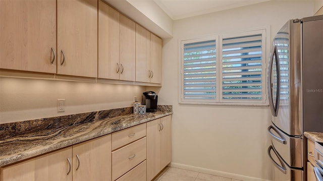 kitchen with stainless steel refrigerator, light brown cabinetry, light tile patterned flooring, and stone counters