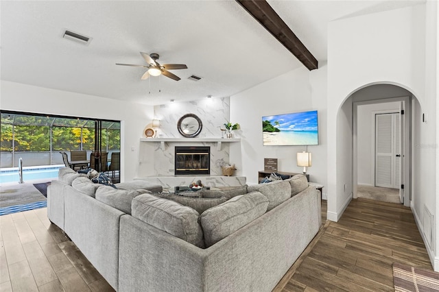 living room with beam ceiling, a high end fireplace, dark wood-type flooring, and ceiling fan