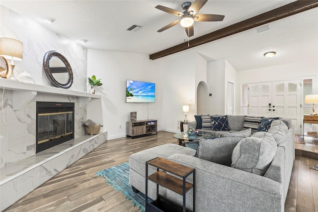 living room with a premium fireplace, ceiling fan, hardwood / wood-style floors, vaulted ceiling with beams, and a textured ceiling