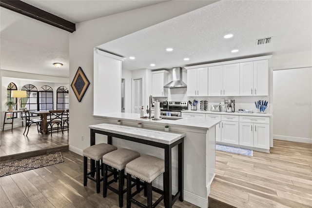 kitchen with wall chimney range hood, light hardwood / wood-style flooring, a textured ceiling, white cabinets, and stainless steel electric stove