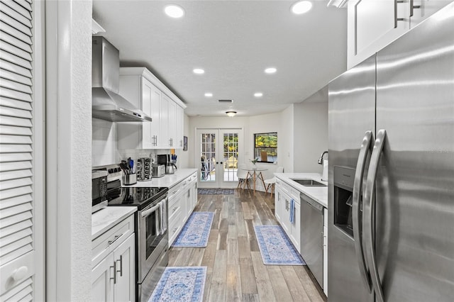 kitchen with french doors, sink, white cabinetry, appliances with stainless steel finishes, and wall chimney range hood