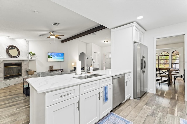 kitchen with appliances with stainless steel finishes, sink, white cabinets, a high end fireplace, and light hardwood / wood-style flooring