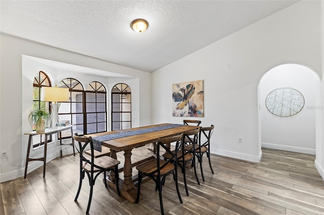 dining space featuring lofted ceiling, wood-type flooring, and a textured ceiling