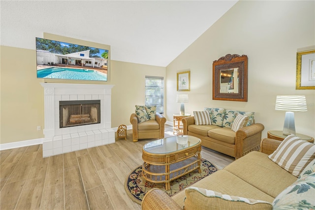 living room featuring lofted ceiling, a tiled fireplace, and wood-type flooring