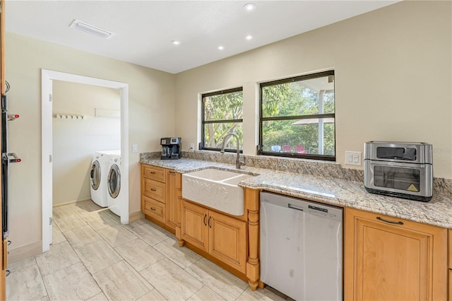 kitchen featuring sink, stainless steel dishwasher, washing machine and clothes dryer, and light stone counters