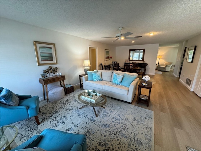 living room with a textured ceiling, ceiling fan, and light wood-type flooring