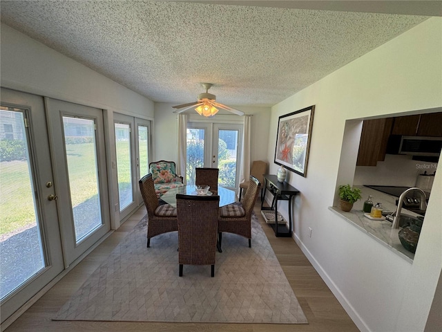 dining space featuring light hardwood / wood-style floors, ceiling fan, french doors, and a textured ceiling