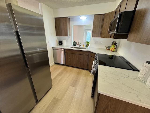 kitchen with a textured ceiling, appliances with stainless steel finishes, light hardwood / wood-style floors, and sink