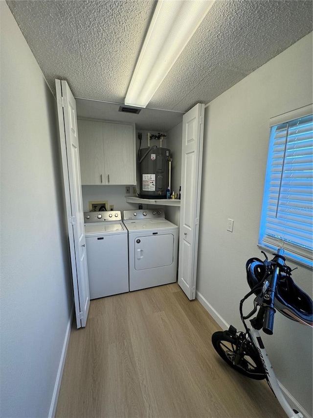 laundry room with washing machine and clothes dryer, a textured ceiling, cabinets, light hardwood / wood-style floors, and water heater