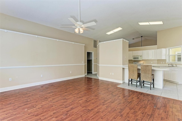 unfurnished living room with vaulted ceiling, ceiling fan, light hardwood / wood-style flooring, and sink