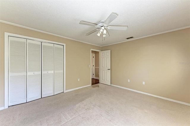 unfurnished bedroom with ornamental molding, ceiling fan, a closet, and light carpet