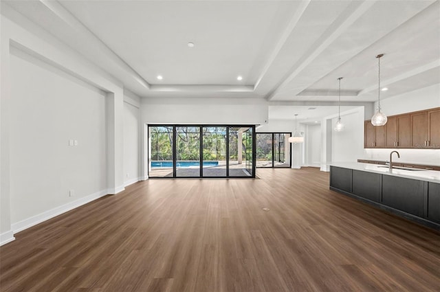 unfurnished living room featuring sink, a tray ceiling, and dark hardwood / wood-style flooring