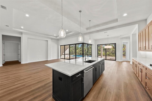 kitchen featuring pendant lighting, light brown cabinetry, sink, a raised ceiling, and a kitchen island with sink