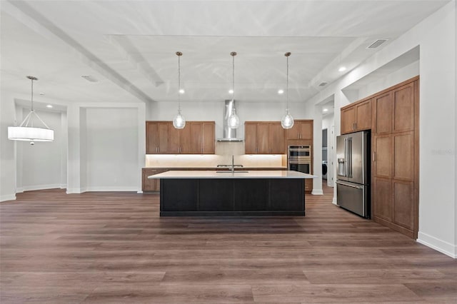 kitchen with appliances with stainless steel finishes, a kitchen island with sink, hanging light fixtures, wall chimney range hood, and sink