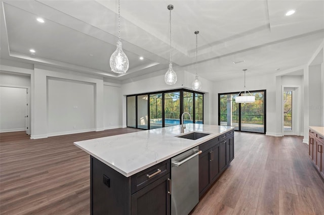 kitchen with a center island with sink, a tray ceiling, decorative light fixtures, dishwasher, and sink