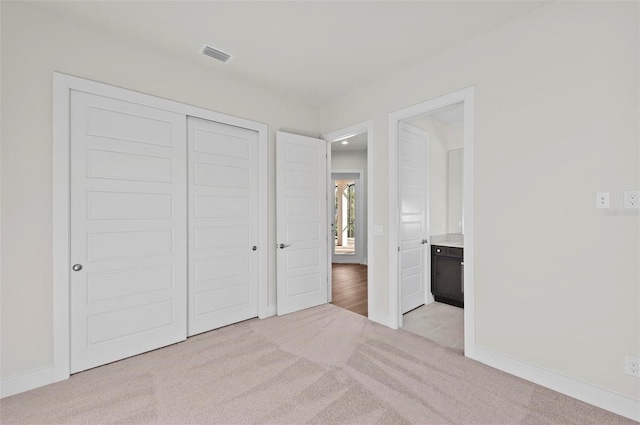 unfurnished bedroom featuring a closet, light colored carpet, and ensuite bath