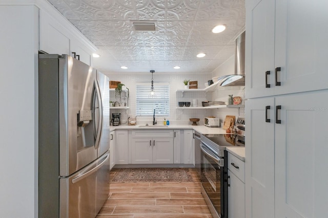 kitchen with white cabinetry, sink, hanging light fixtures, stainless steel appliances, and wall chimney exhaust hood